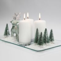 Juldekoration med ljus, renar, granar och snö på glasfat